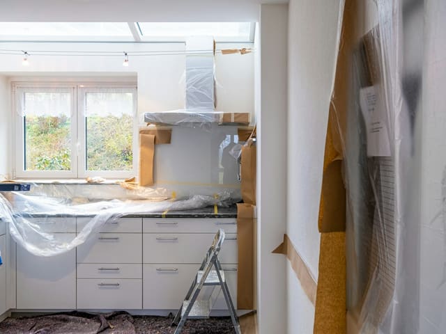 Kitchen mid-renovation with new white cabinets going in and a step ladder by the window